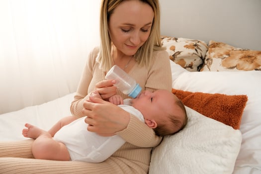mom feeds a newborn baby with a bottle. the sun is shining in the background. photo