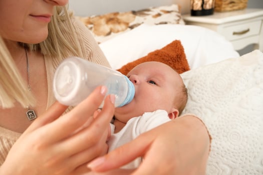 mom feeds a newborn baby with a bottle. the sun is shining in the background. photo
