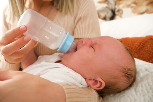mom feeds a newborn baby with a bottle. the sun is shining in the background. photo