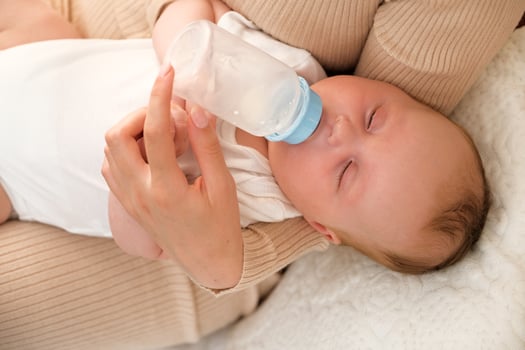 mom feeds a newborn baby with a bottle. the sun is shining in the background. photo