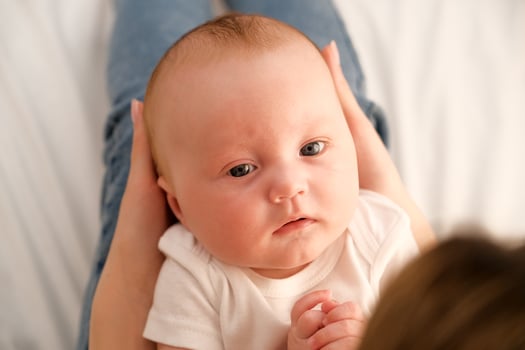 mom holds a newborn baby in her arms. in the background the sun shines from the window. photo