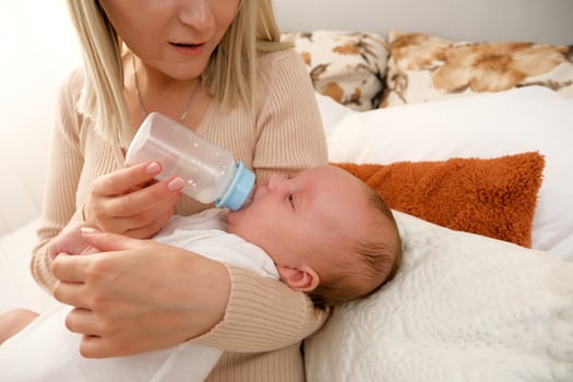 mom feeds a newborn baby with a bottle. the sun is shining in the background. photo