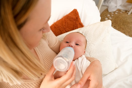mom feeds a newborn baby with a bottle. the sun is shining in the background. photo