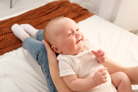 mom holds a newborn baby in her arms. in the background the sun shines from the window. photo
