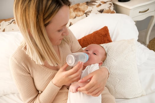 mom feeds a newborn baby with a bottle. the sun is shining in the background. photo
