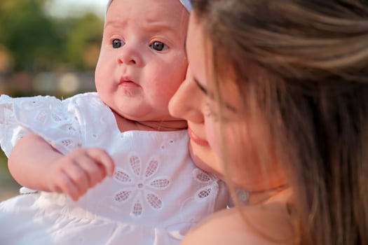 a beautiful girl in a white dress with a newborn baby is sitting on the beach, on the sand. photo
