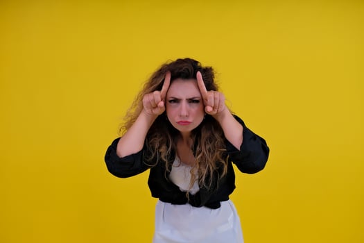 beautiful girl on a yellow background. Pretty brave woman showing wild devilish side making bull horns with her fingers on her head. photo