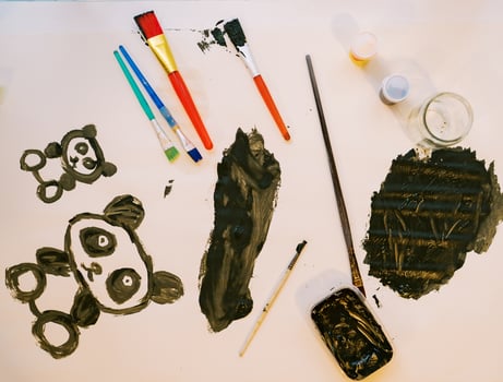 Two panda bears painted on a white sheet next to brushes and jars of paint photo