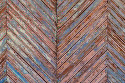 old wooden planks gate chevron pattern texture with peeled brown and blue paint layers under sun-bleached blue paint layer photo