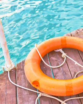 Orange lifebuoy with rope on a wooden pier near sea. Close up of lifebuoy on wooden pier at the beach. photo