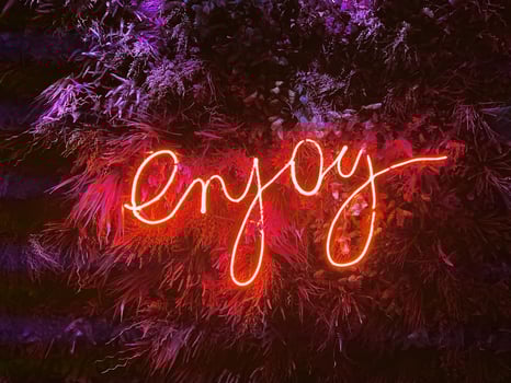 LED sign Enjoy. Live neon sign on the leaves wall background. photo