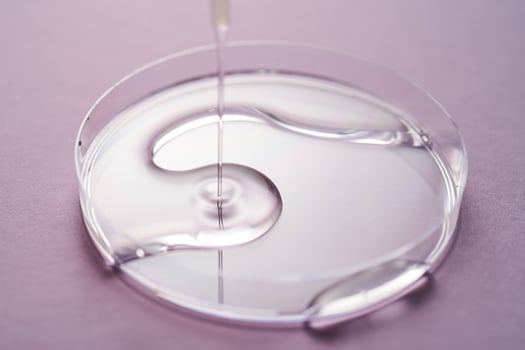 Serum or cosmetic oil flows into a transparent bowl on a purple background. photo