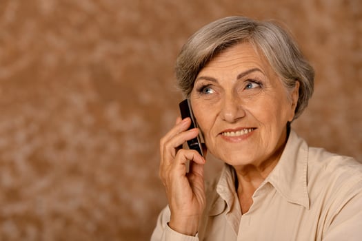 Elderly woman talking on mobile phone on beige photo