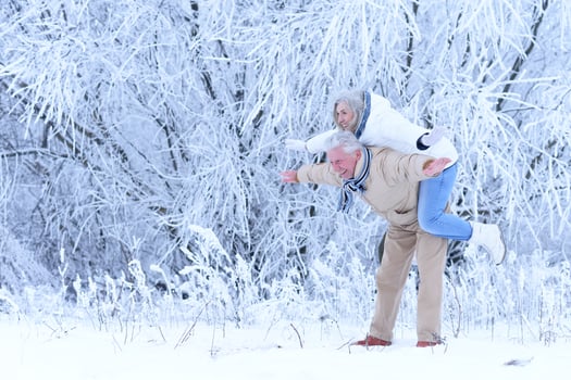 Elderly man holding an old woman on his back in winter park photo