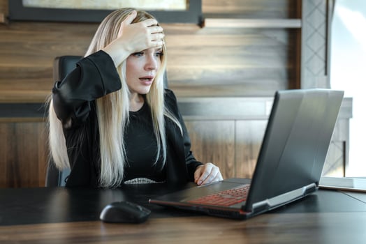 Businesswoman with frightened expression looks at laptop screen, clutching her forehead with her hand in surprise photo