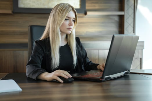 Blonde girl in business clothes sits in front of laptop in office and works intently, concept of online education and work. photo