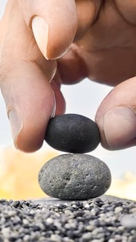 Hand of man places black stone on gray stone creating a pyramid, zen concept, vertical frame. photo