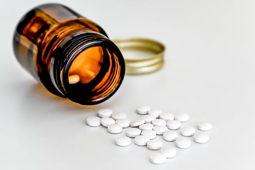 White Pills Scattered on Table Next to Brown Glass Vial, on White Background, Close-up photo