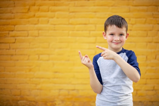 Smiling cute kid pointing with finger aside on yellow brick wall background photo