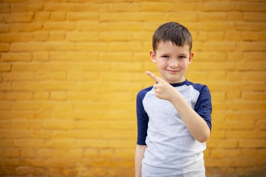 Smiling cute kid pointing with finger aside on yellow brick wall background photo