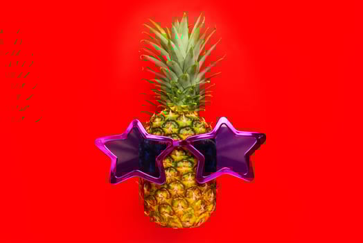 Pineapple with sunglasses on red background. Pineapple in star glasses. photo