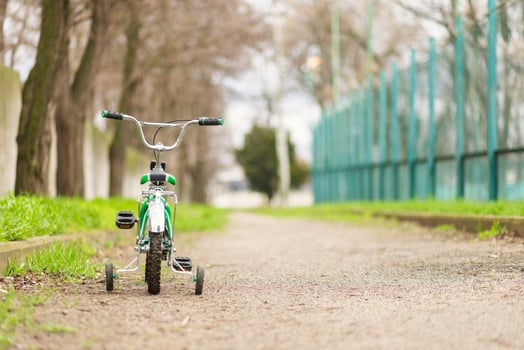 A green bicycle for children with additional wheels at road in park photo
