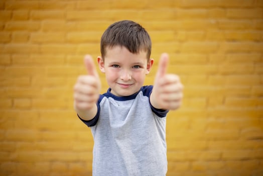 Smiling Boy Giving Thumbs Up Against Yellow Wall photo