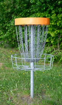 A disc golf basket with chains sits on a grassy field, surrounded by trees photo