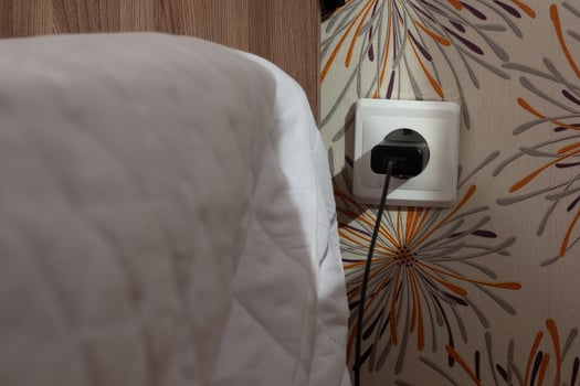 Wall socket with charger plug inside close to bed photo