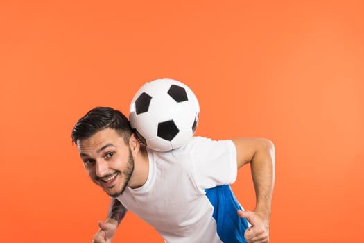 Football player do tricks with ball isolated on orange background photo