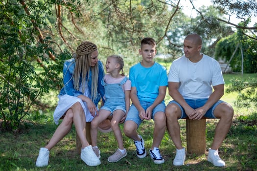 A family sits on a bench, in a green forest setting, all dressed in casual summer attire. perfect for content on family dynamics, bonding, and the value of spending time together. photo