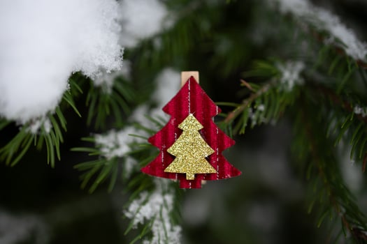 Red Christmas ornament in shape of fir tree on snow-covered Christmas tree branch outdoors. Selective focus, close-up photo