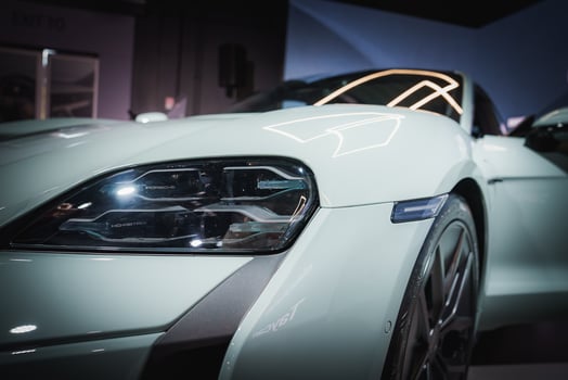 Sleek, modern car in glossy white finish. Close up of front left side reveals luxury design, LED headlight, and alloy wheel. Indoor setting with ambient lighting. photo