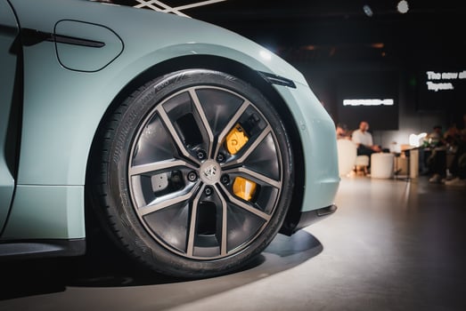 High performance luxury car wheel with yellow brake caliper close up. Multi spoke design, low profile tire. Blue car. Indoor showroom with visitors. New model signage. Exhibition setting. photo