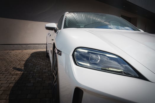 Modern white car close up with sleek design, clear headlight, and glossy surface. Parked on cobblestone with urban background. Bright natural light highlights luxury and elegance. photo