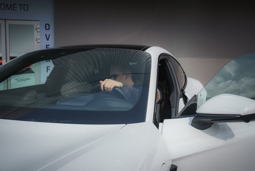 Close up view of white car with driver's side door ajar, hand gripping steering wheel. Sleek modern car in showroom setting. photo