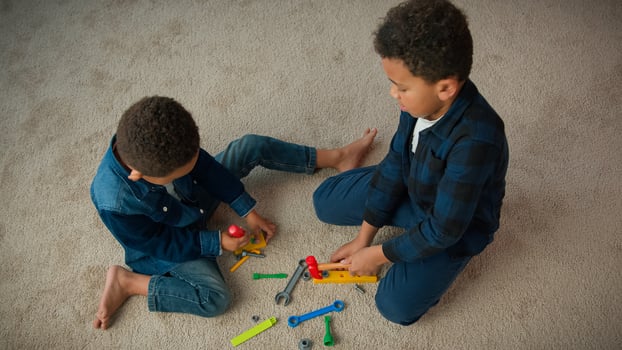 Top view two little siblings boys African American friends kids schoolboys children play game sit on carpet in living room at home playing with plastic toys repair tools hummer screwdriver spanner photo