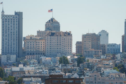 Daytime view of San Francisco's urban landscape. Iconic hilly terrain with buildings of varying heights. Dominant building with peaked roof and flag. Storied city architecture. photo