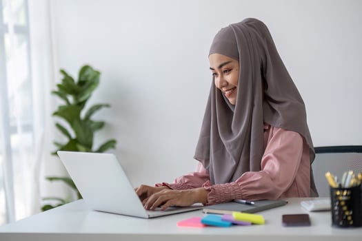 Smiling Muslim business woman Wearing a hijab while chatting online on a work desk in the office. photo