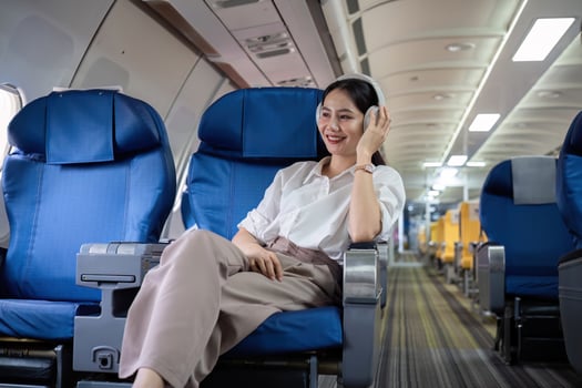 Young woman wearing headphones listening to music during travel, sitting near window in first class on airplane during flight, travel and business concept photo