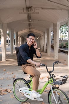 A young Asian businessman rides a bicycle to work. Standing outside the office talking on the phone and talking about business. Concept of reducing energy and reducing air pollution. photo