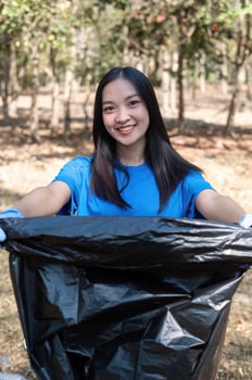 A cute young woman holds a garbage bag and a group of Asian volunteers collect garbage in plastic bags and clean up the area in the forest to preserve the natural ecosystem. photo
