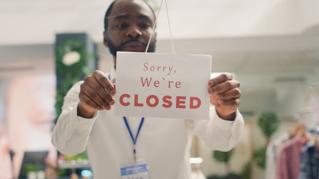 African american man working in trendy clothing store closing it at night. Tired BIPOC retail clerk turning opened message sign on fashion boutique door in mall at shift end photo