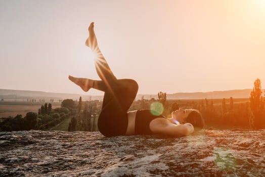 Fitness woman. Happy middle-aged fitness woman doing stretching and pilates on a rock near forest at sunset. Female fitness yoga routine. Healthy lifestyle with focus on well-being and relaxation. photo