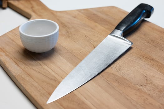 A knife, wooden cutting board, and bowl sit on a kitchen counter, ready for meal preparation to begin. photo