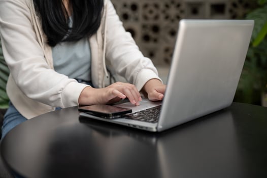 A cropped image of an Asian woman working on her laptop while sitting at an outdoor table of a cafe. photo