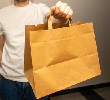 courier holds paper bag and phone with white blank screen and inscription, order delivery concept, online shopping photo