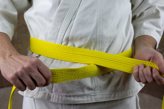 Kyokushinkai karate athlete ties yellow belt around his waist, adjusting martial arts equipment, senior student yellow belt photo