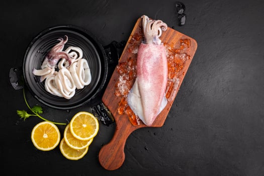 Fresh raw squid. Raw squid on a black plate with ice. Lemon slices. Top view and copy space for your text. photo