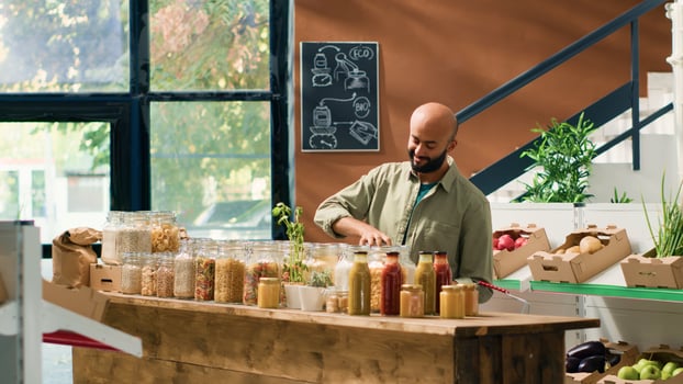 Middle eastern man in ecological food store examining organic homegrown fruits and vegetables, opening jars with sustainable pasta or spices. Customer admires fresh bio merchandise. photo